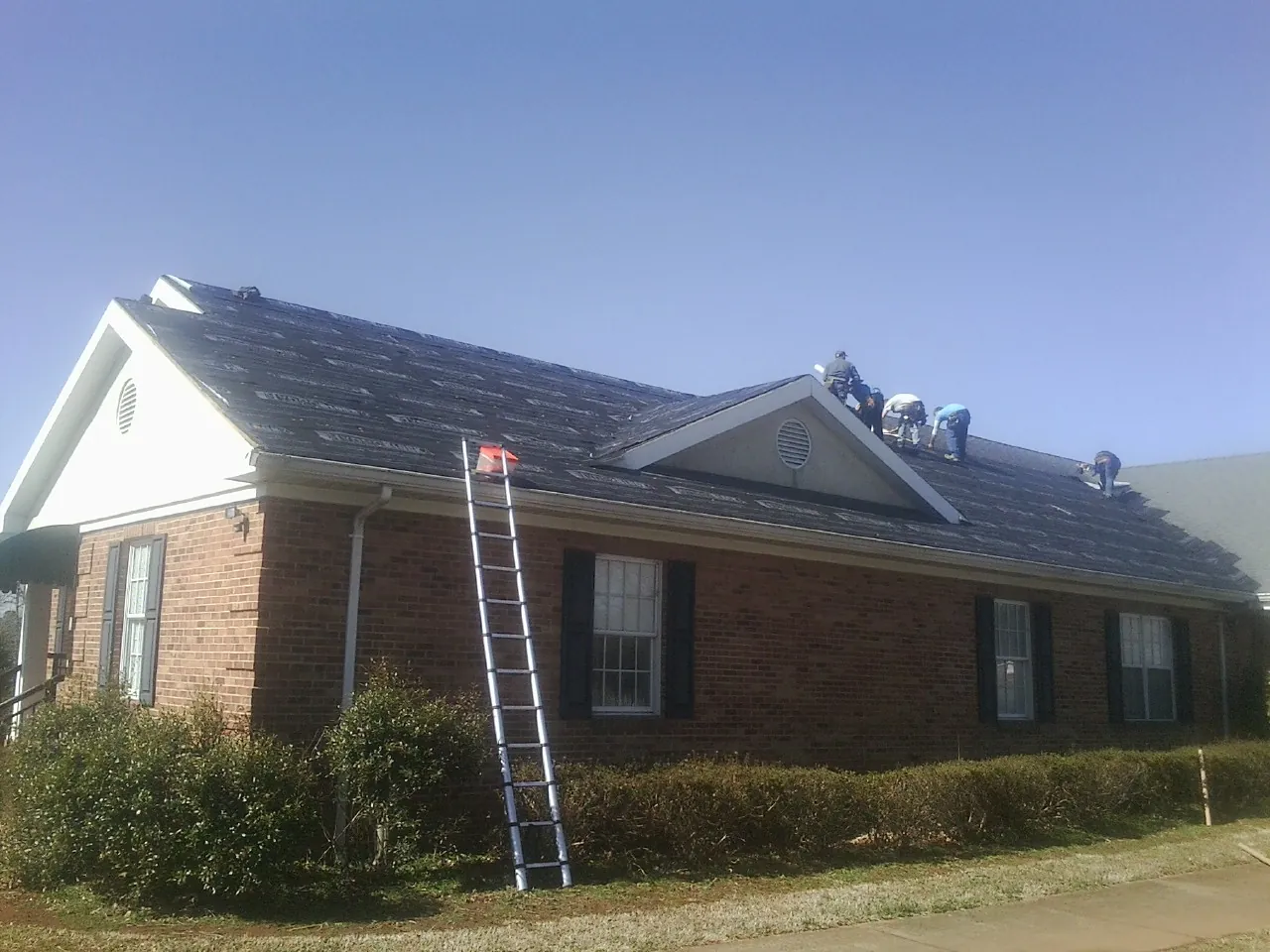 Crew tearing shingles off a brick ranch roof with a ladder set — Emergency Roof Repair work by our crew in Flemington