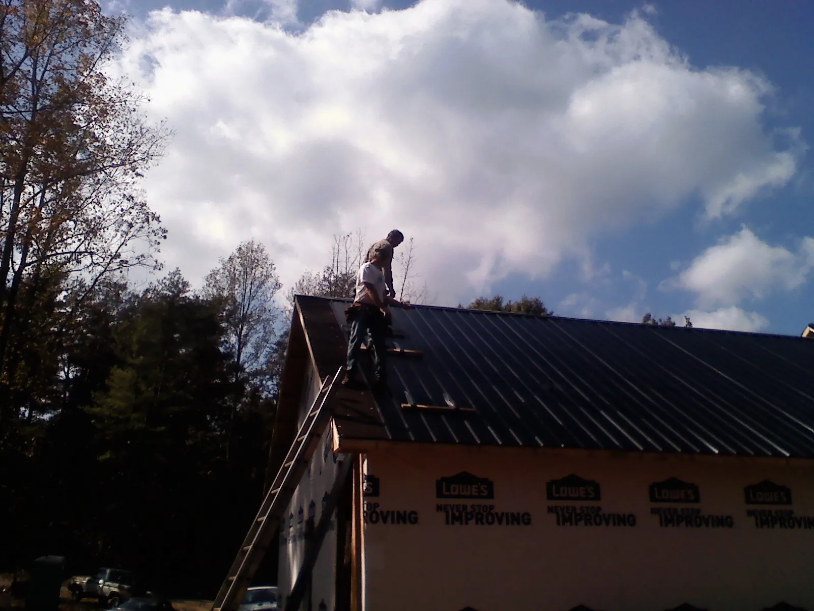 Roofer fastening dark metal panels high against a cloudy sky, from a Roof Inspection job in Flemington